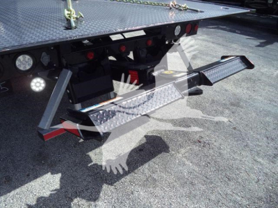 Truck rear showing fold-out aluminum step and platform with textured steps, side underride guard, and hydraulic or support brackets for a rollback trailer.