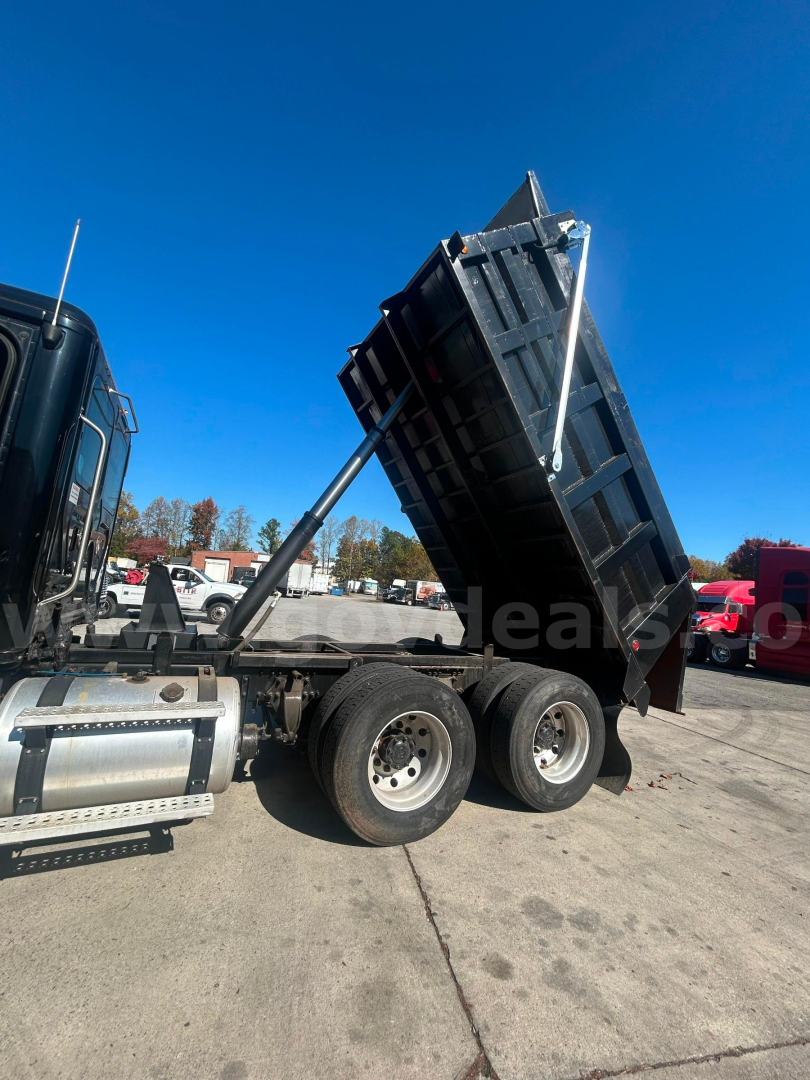 Dump bed truck rear view showing raised dump bed on Freightliner Cascadia with three axles and hydraulic lift.