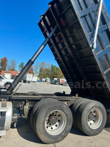 Dump truck bed raised on a Freightliner Cascadia 125 dump truck showing dual rear wheels and hydraulic lift cylinder.