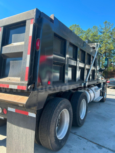 Dump truck side view showing Freightliner Cascadia 125 bed with dual rear axles and black dump body.