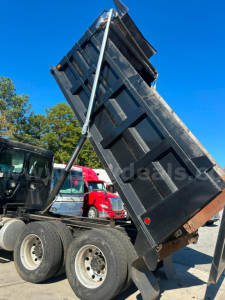 Dump truck bed raised on a Freightliner Cascadia 125 dump truck showing hydraulic cylinder and black dump bed with a red taillight and dual rear wheels.
