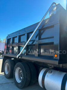 Freightliner Cascadia dump truck side view showing dump bed and hydraulic strap rupture kit, dual rear axles and wheel tires.
