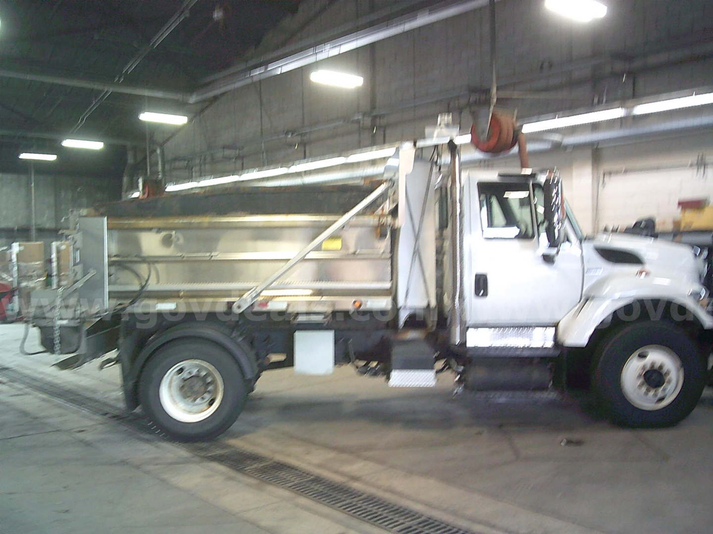 Truck side view of a 2010 International WorkStar 7400 dump truck in a warehouse showing the cab, dump bed, and front wheel.