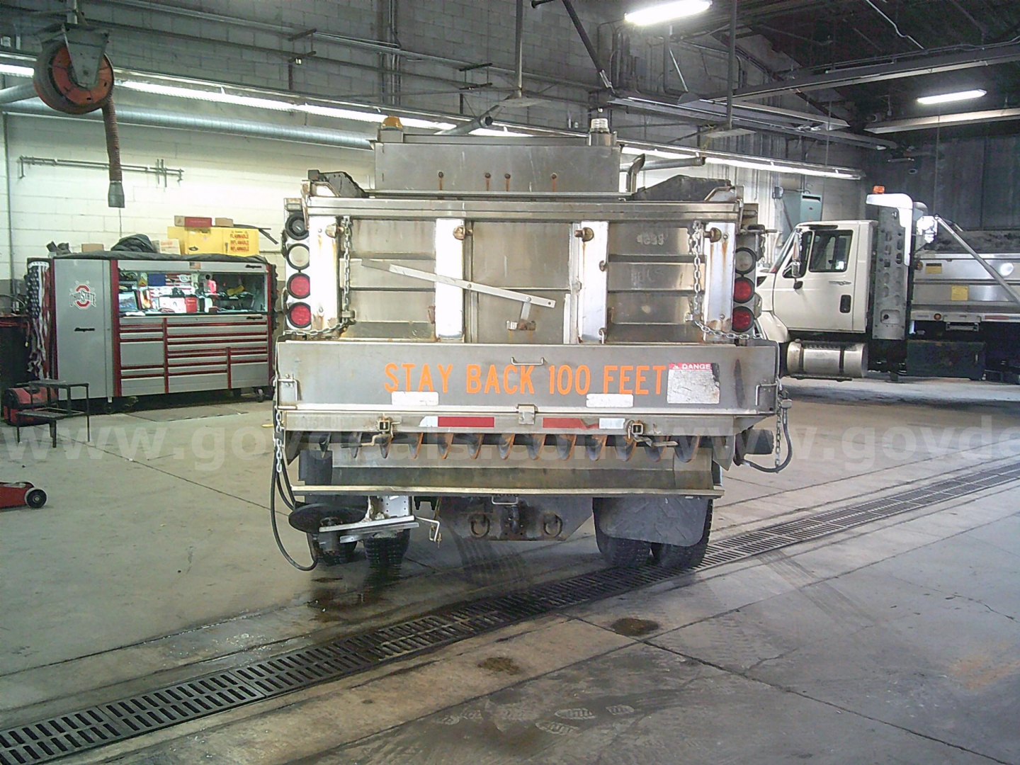 Dump truck rear view showing 'STAY BACK 100 FEET' decal and taillights in an indoor service bay.