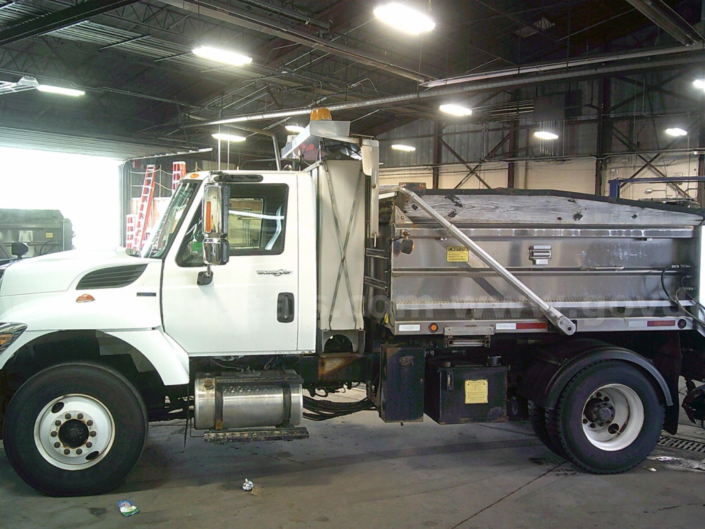 Side view of a white 2010 International WorkStar 7400 dump truck inside a warehouse. Visible text includes VIN 1HTWDAAR3AH249366 and stock number 443-2638 on signage.