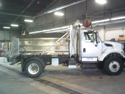 Truck side view of a 2010 International WorkStar 7400 dump truck in a warehouse showing the cab, dump bed, and front wheel.