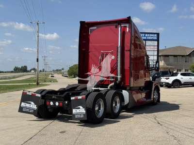 Kenworth T680 semi-truck from rear side view showing sleeper cab, red paint, dual rear axles, and chassis with fifth-wheel area.
