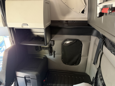 Cab interior of a Freightliner PT126064ST showing storage drawers, a small black pouch on the wall, and a ribbed floor panel.