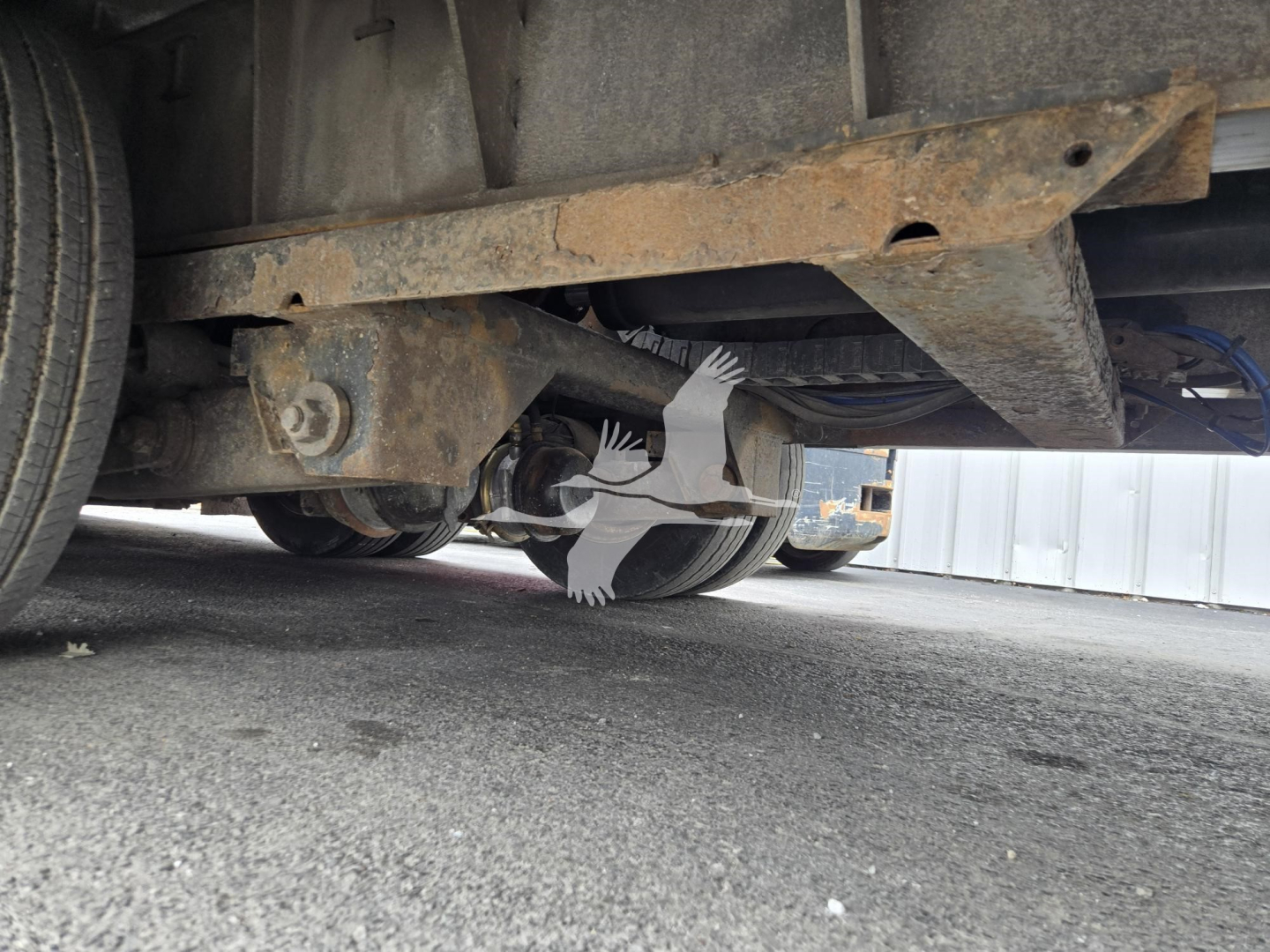 Traveling axle trailer underside showing rusted steel frame with suspension components and wheels.