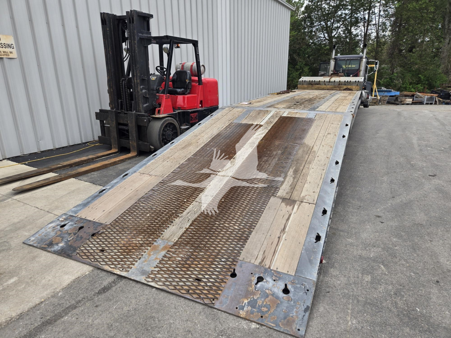 Flatbed trailer with steel deck and perforated ramp sections showing wear and rust patterns, 2011 Landoll model 93051-15, located outdoors with forklift in background.