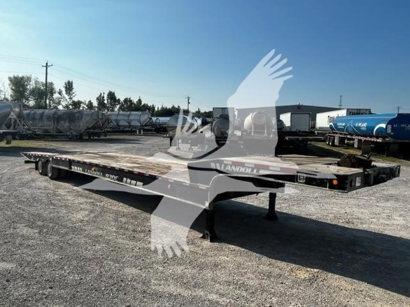Trailer axle device showing Landoll 2011 model flatbed trailer with low deck, dual axles, and landing gear in an outdoor lot.