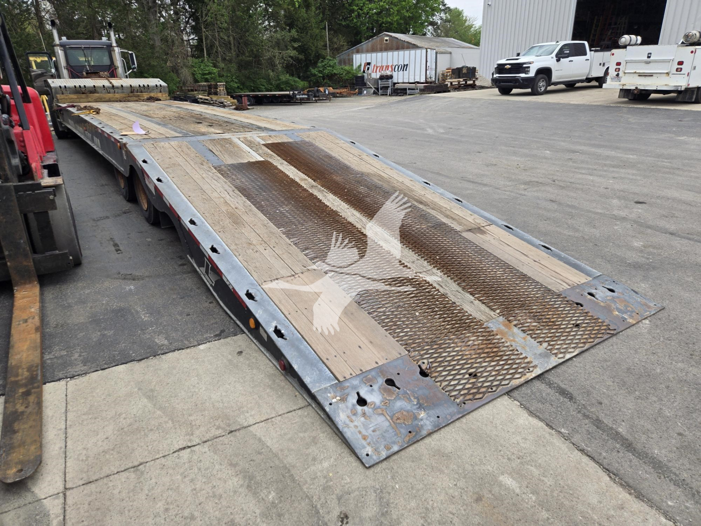 Tow trailer deck with steel grate ramp, weathered metal surface showing hoses and safety markings.
