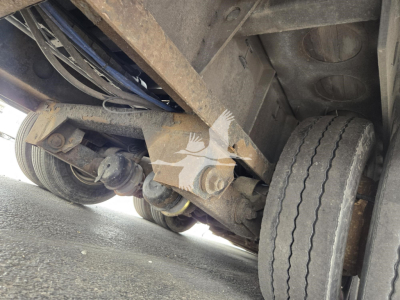 Traveling axle trailer undercarriage showing dual rear wheels and suspension components with rusted frame and undercarriage hardware.