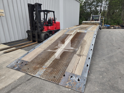 Flatbed trailer with steel deck and perforated ramp sections showing wear and rust patterns, 2011 Landoll model 93051-15, located outdoors with forklift in background.