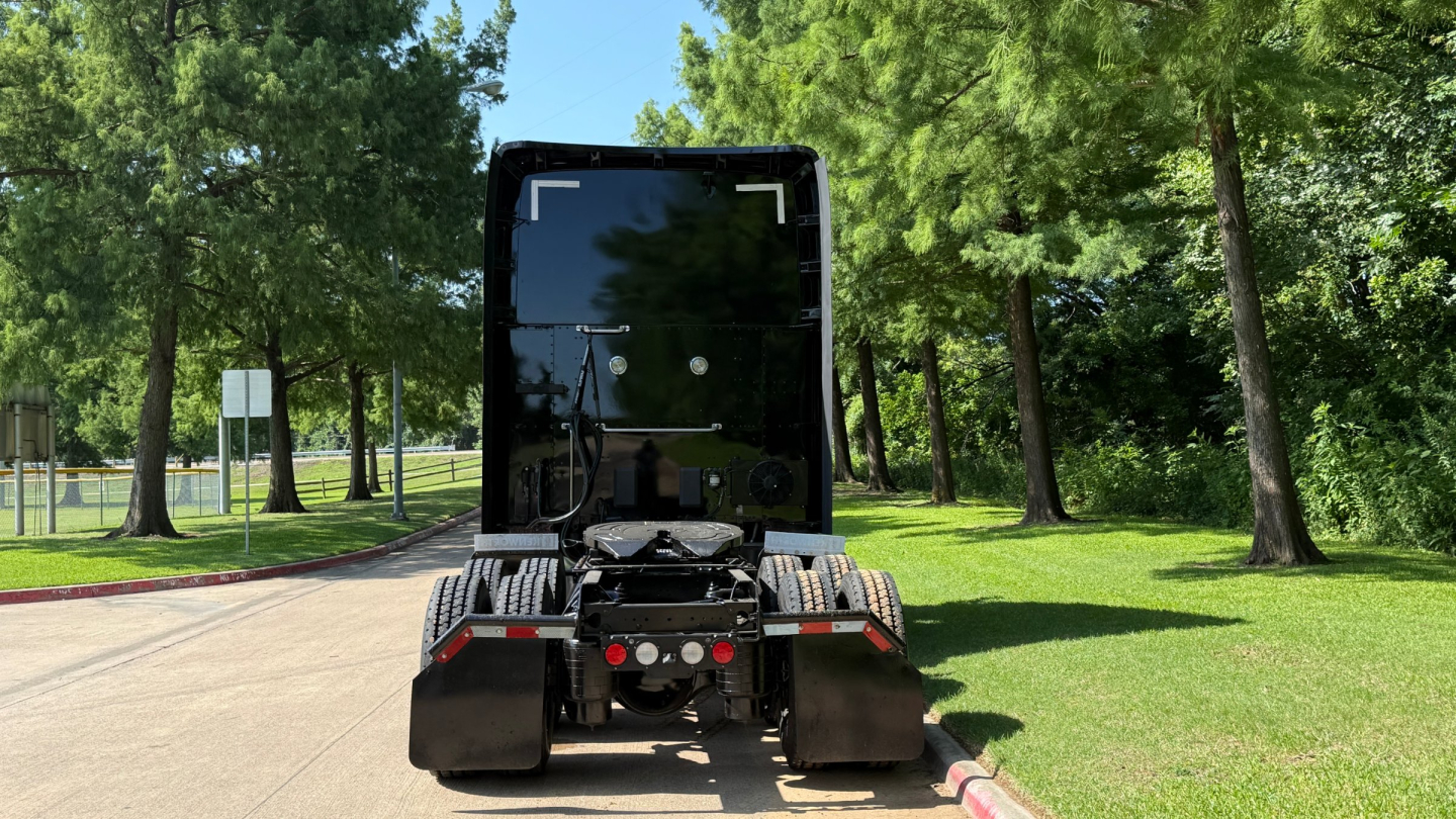 Kenworth T680 tractor rear view showing fifth wheel, dual rear wheels, and fender mirrors in a grassy outdoor lot.