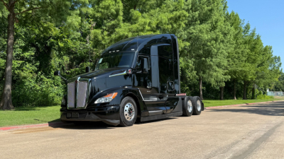 Kenworth T680 tractor-trailer in black, front left view, showing cab and sleeper with three axles, daytime outdoor setting