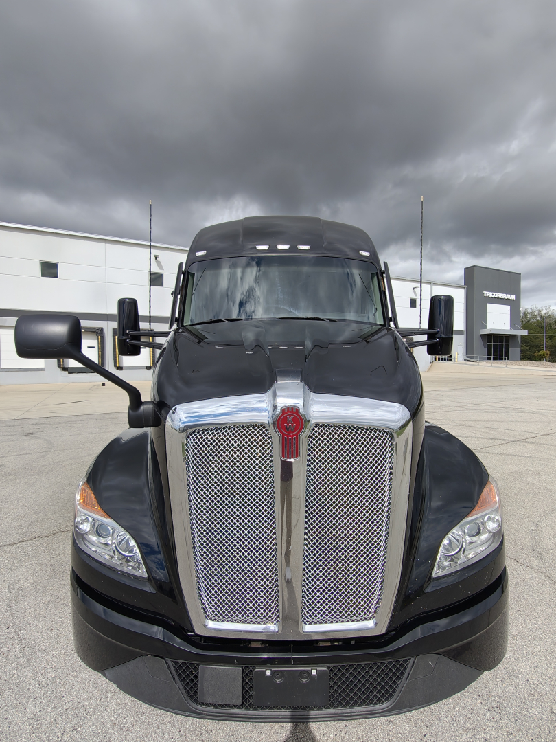 Kenworth T680 front view showing large chrome grille with center crest and black hood, headlights, and side mirrors.
