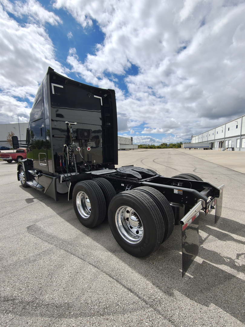 Kenworth T680 truck chassis and sleeper cab viewed from rear-left, with dual rear axles and fifth-wheel area visible; black paint, chrome wheels, clear sky.