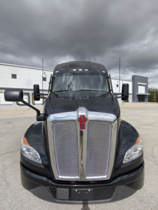 Kenworth T680 front view showing large chrome grille with center crest and black hood, headlights, and side mirrors.
