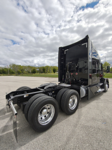 Kenworth T680 tractor cab with black sleeper, dual rear axles, side view showing fuel tanks and chrome wheels.