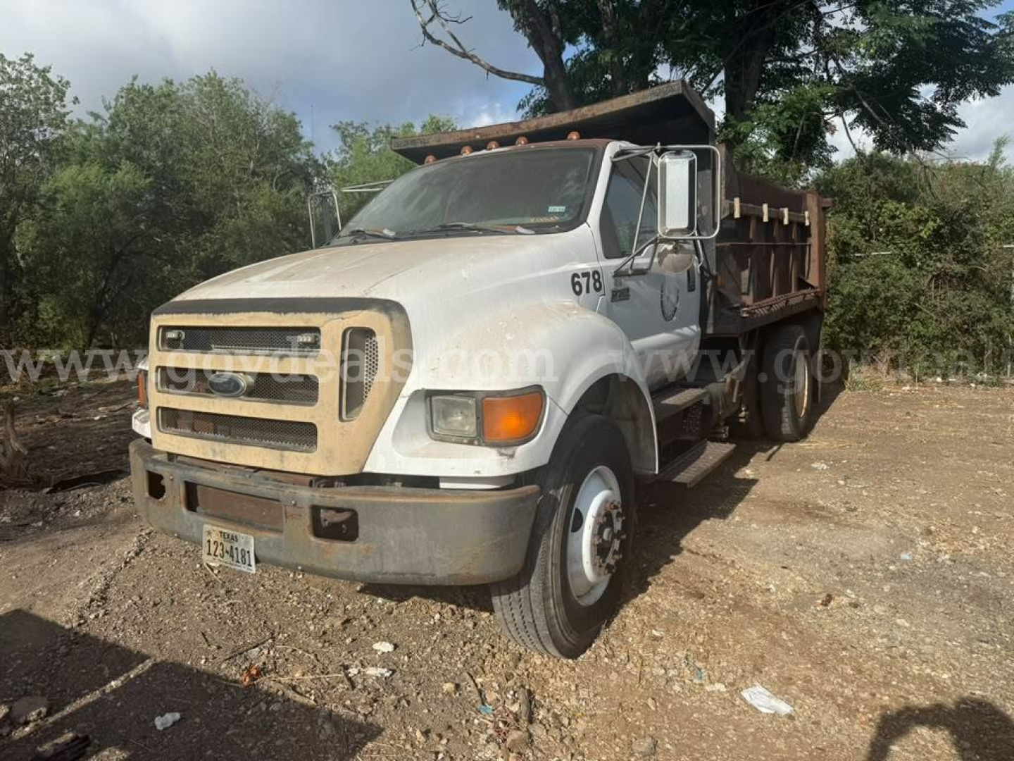 2005 Ford F-750 dump truck in-service view showing front grille, bumper, hood, cab with number 678, and dumped bed at a dusty lot.