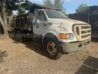 Ford F-750 dump truck shown in a yard with dirt lot, white cab, front grille, and brown dump body; number 678 on door; visible wear and dirt on body.