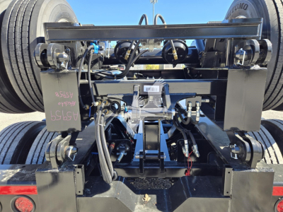 Trailer flip axle hydraulic system showing frame, hoses, hoses, and hydraulic components with wheels in background.