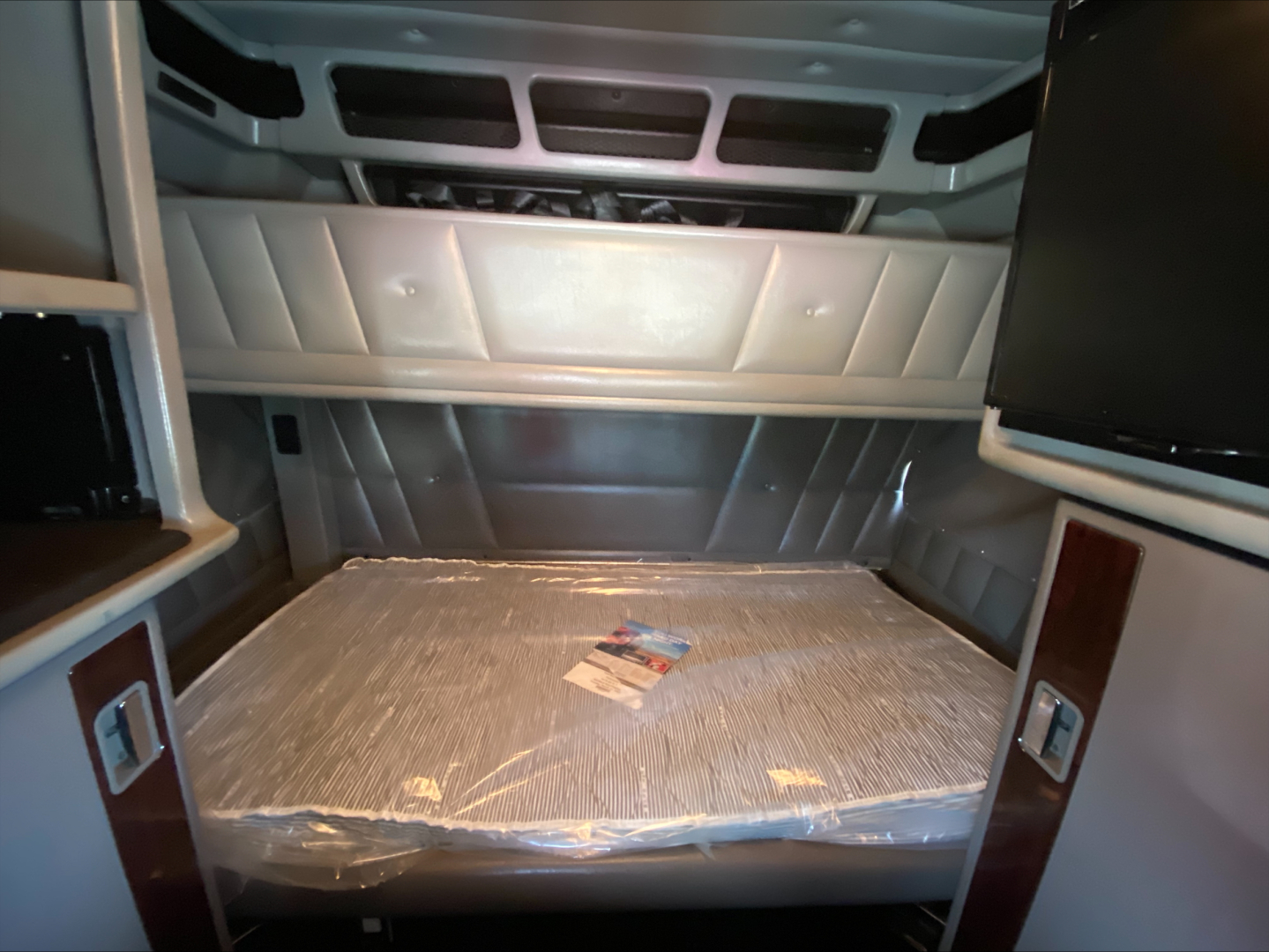 Conventional sleeper truck cab interior with sleeper berth; raised bed with plastic cover and overhead storage panels.