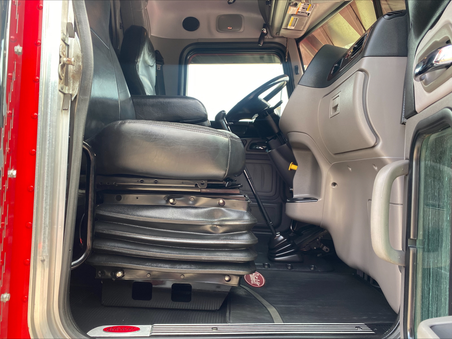 Peterbilt 389 cab interior view from doorway showing driver seat and dashboard; steering wheel, pedals, and floor mat visible