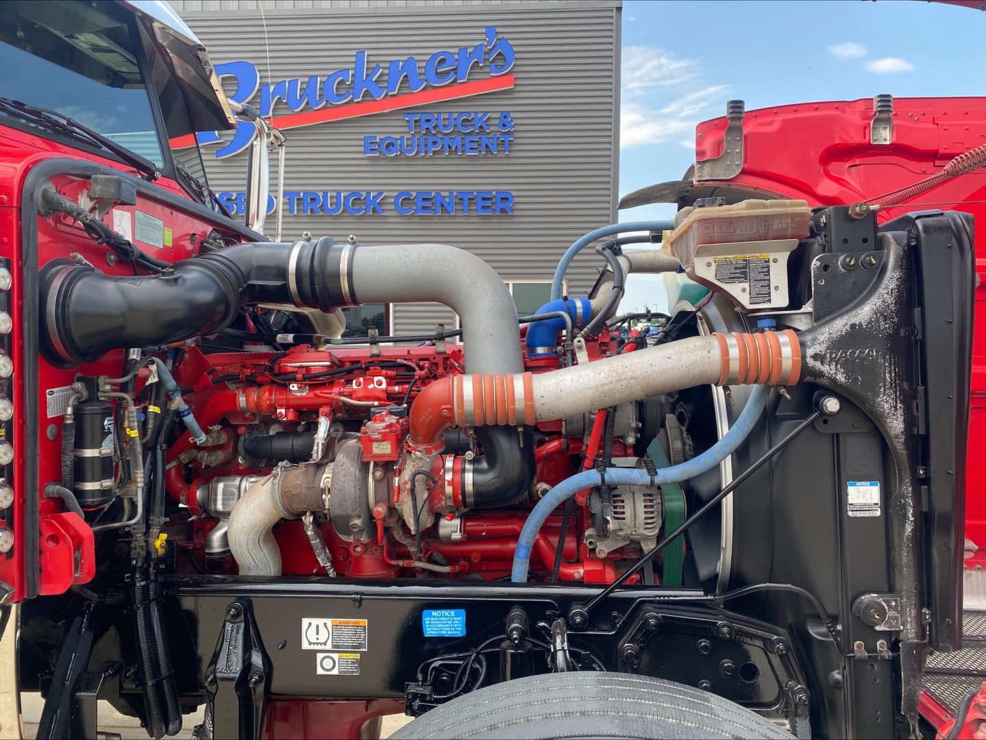 Peterbilt engine bay in a 2021 truck showing red engine block, large intake hoses, blue coolant hose, and radiator with fan shroud.