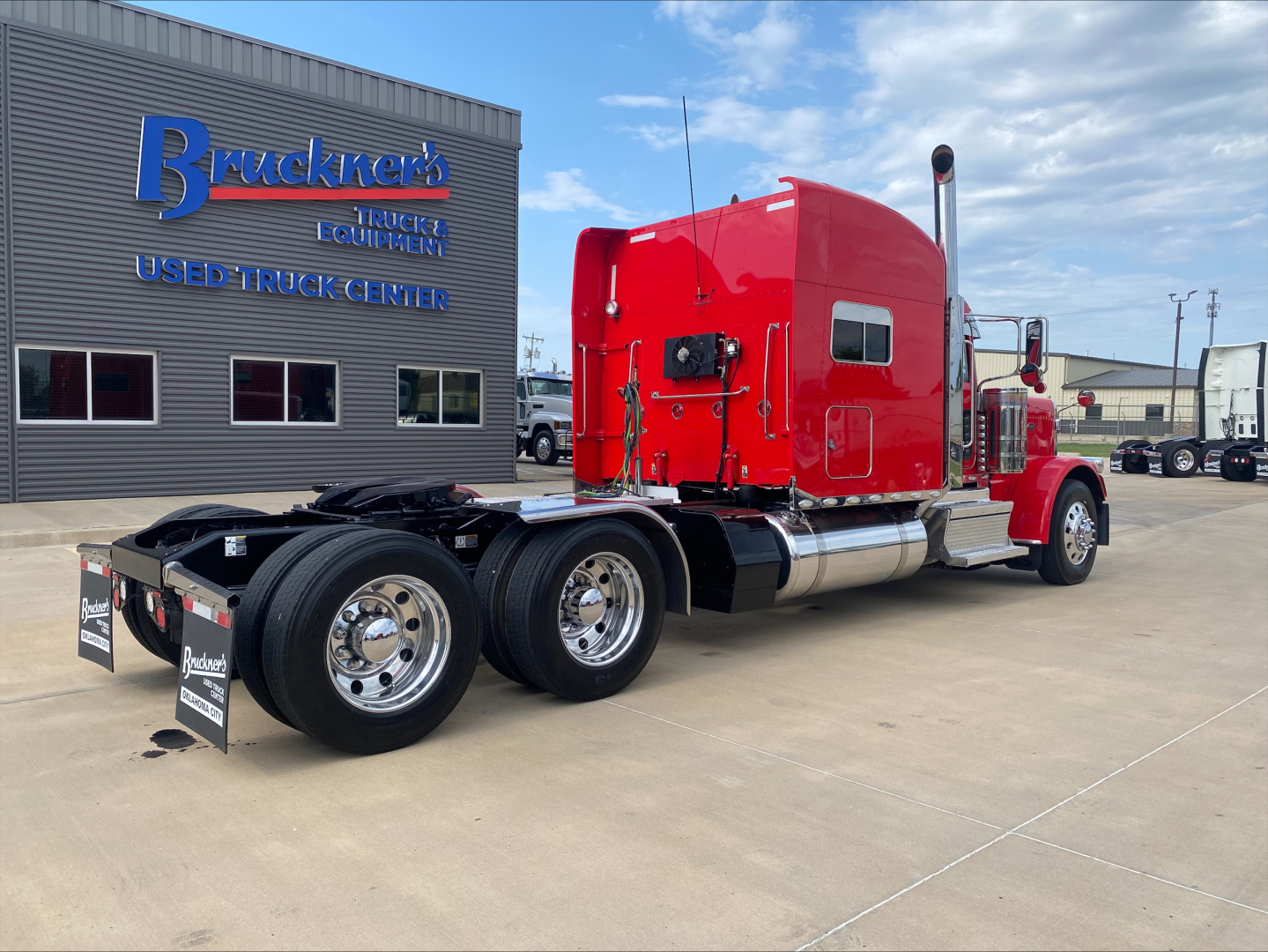 Peterbilt 389 tractor cab with red paint in-service showing chrome fuel tanks and dual rear axles.