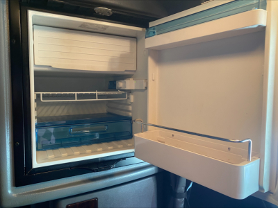 Fridge/freezer in a Peterbilt 389 cab interior showing empty shelves and freezer compartment with drawer front, open door, and storage trays.