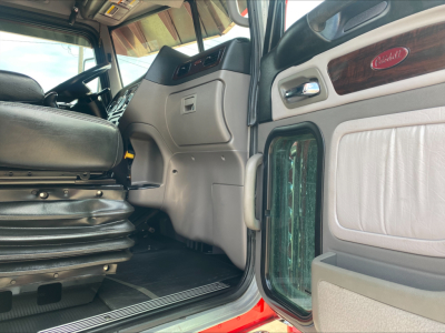 Truck cab interior view of a Peterbilt 389 showing the driver's seat, dashboard, and door panel with Peterbilt emblem.