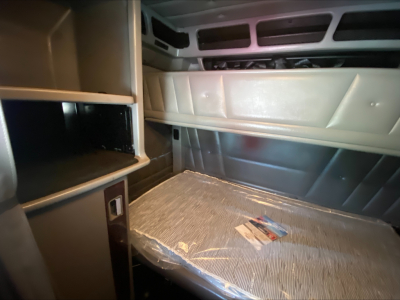 Peterbilt 389 sleeper cab interior shelf and dash area showing storage cabinet and window panel with plastic-wrapped floor mat.