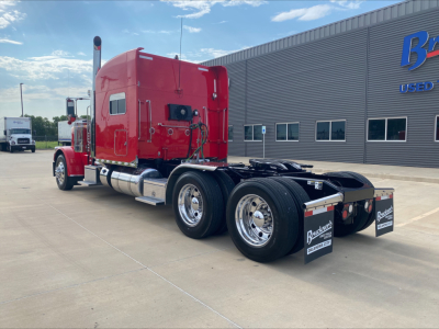 Peterbilt 389 tractor with red cab, viewed from rear-left, showing dual rear axles and fifth wheel on a dealership lot.
