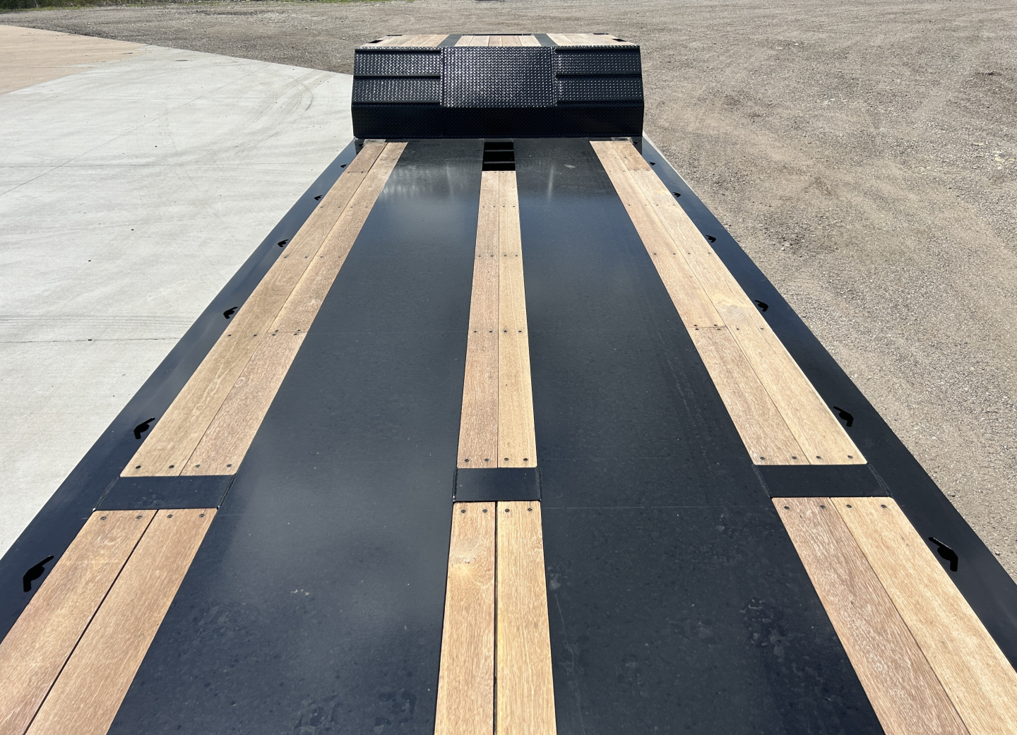 Trailer deck view showing lowboy platform with wooden boards and steel beams, front ramps in distance.