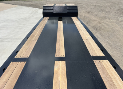 Trailer deck view showing lowboy platform with wooden boards and steel beams, front ramps in distance.