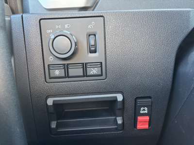 Dashboard switch panel and storage compartment in a Mack AN64T cab showing headlight dial, control buttons, and a red hazard/lock switch.