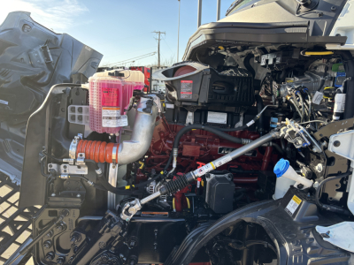 Mack AN64T truck engine bay showing coolant reservoir, pink coolant overflow tank, hoses, wiring, and engine components.