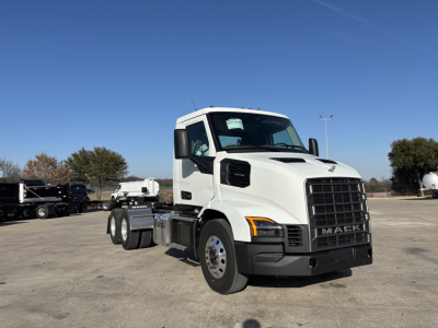 New white 2027 Mack AN64T conventional daycab truck in a parking lot, front three-quarter view with large grille and Mack logo, no visible text other than vehicle branding.
