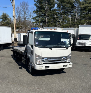 Isuzu NRR box truck with cab and flatbed in a dealership lot, front view, white with blue light bar on roof.
