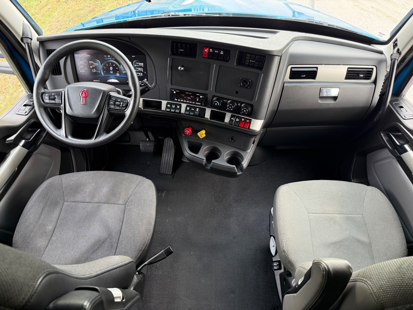 Kenworth T680 cab interior showing steering wheel, dashboard, and front seats; center console with gauges and controls visible.