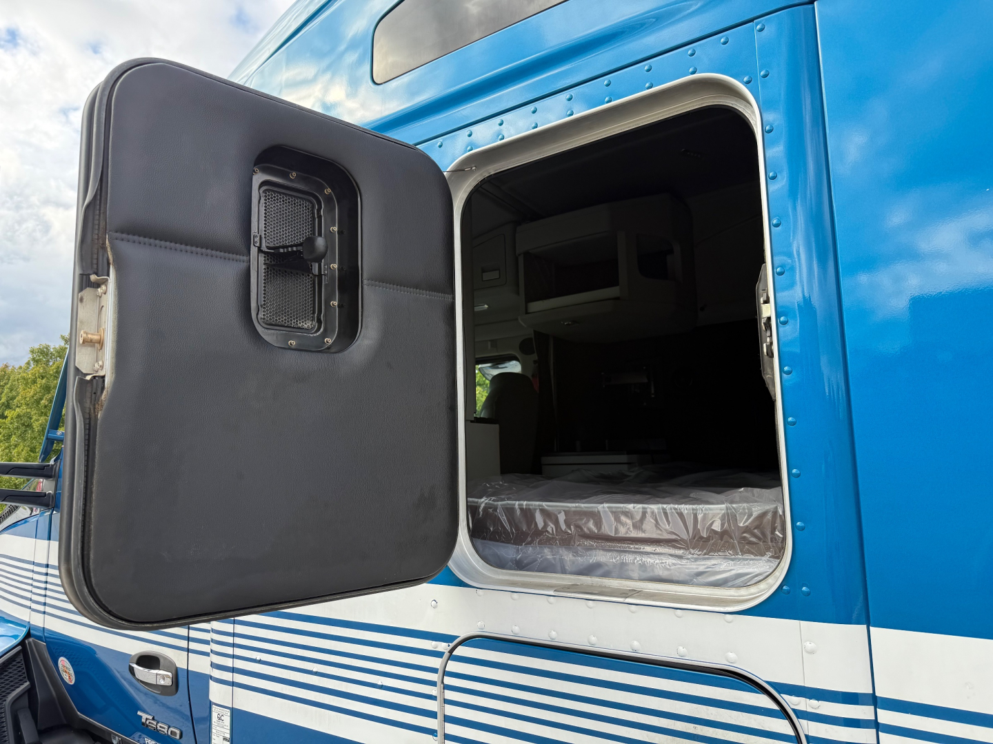 Kenworth T680 truck door open showing sleeper cab interior and black door panel with small window vent.