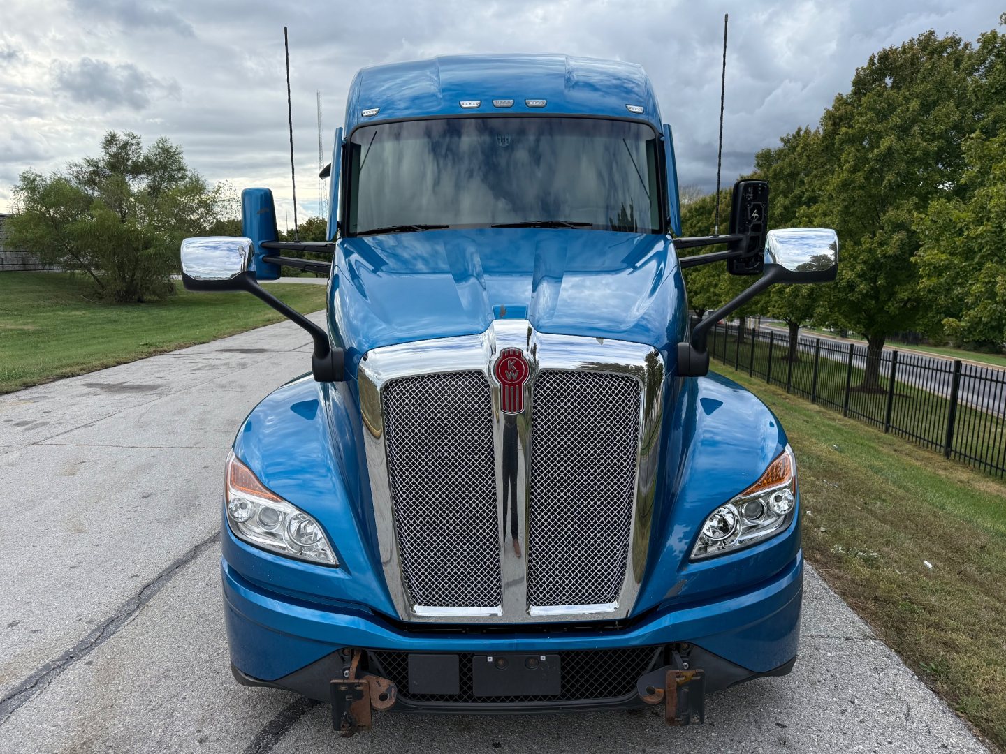 Blue Kenworth T680 front view with chrome grille and headlights, large mirrors; no text visible on image beyond reflections.
