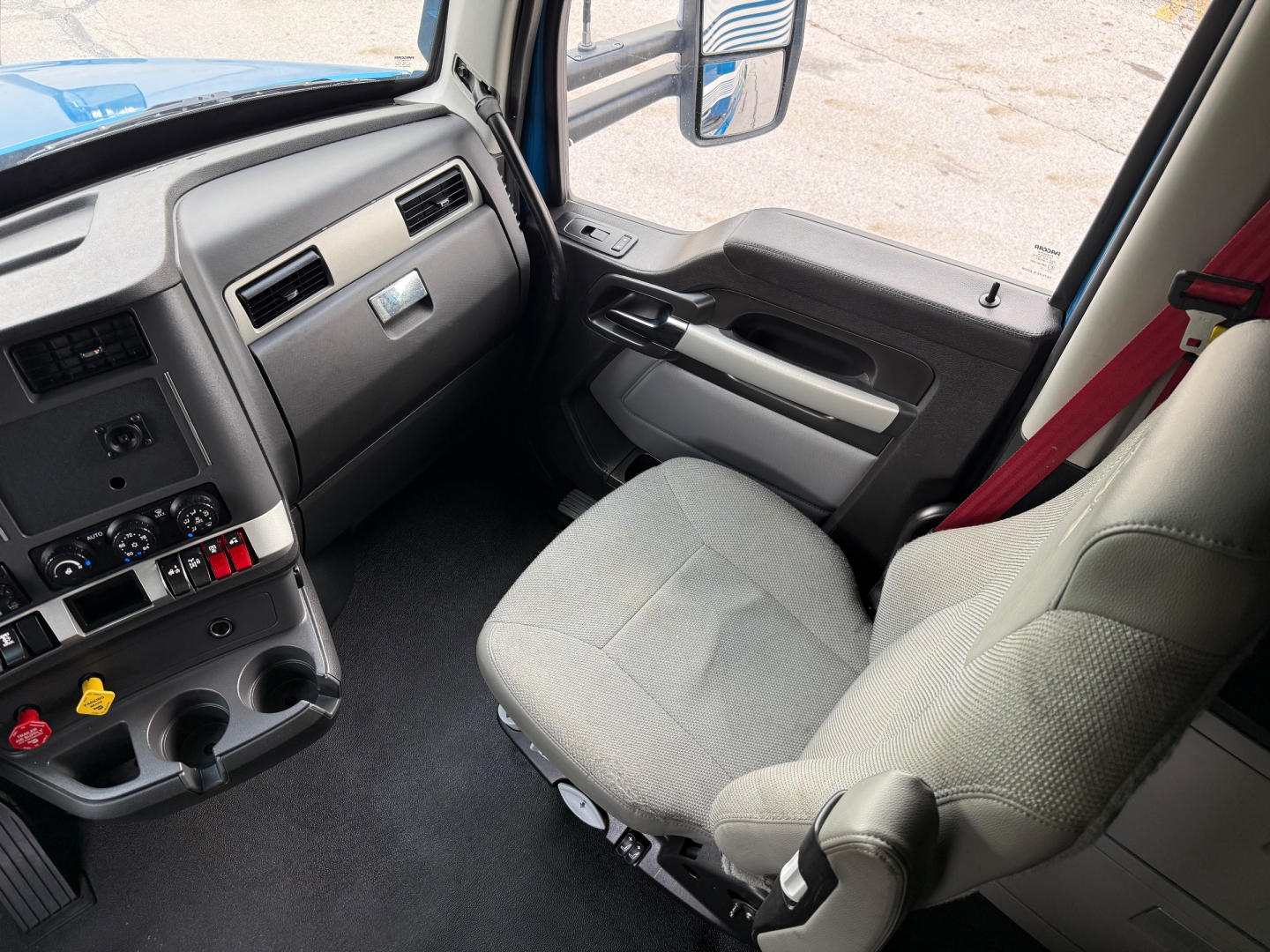 Kenworth T680 truck interior driver seat and dashboard view showing steering wheel, center console, and door panel.