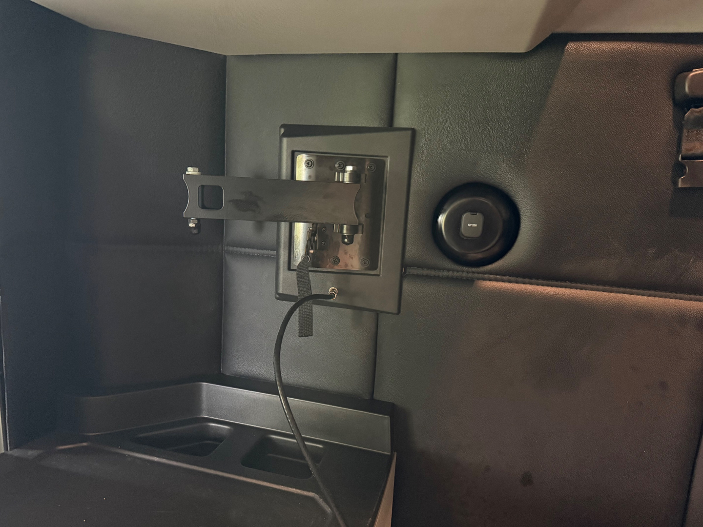 Kenworth T680 interior storage with a small mounted panel and circular power outlet, showing a loose cable and interior paneling.