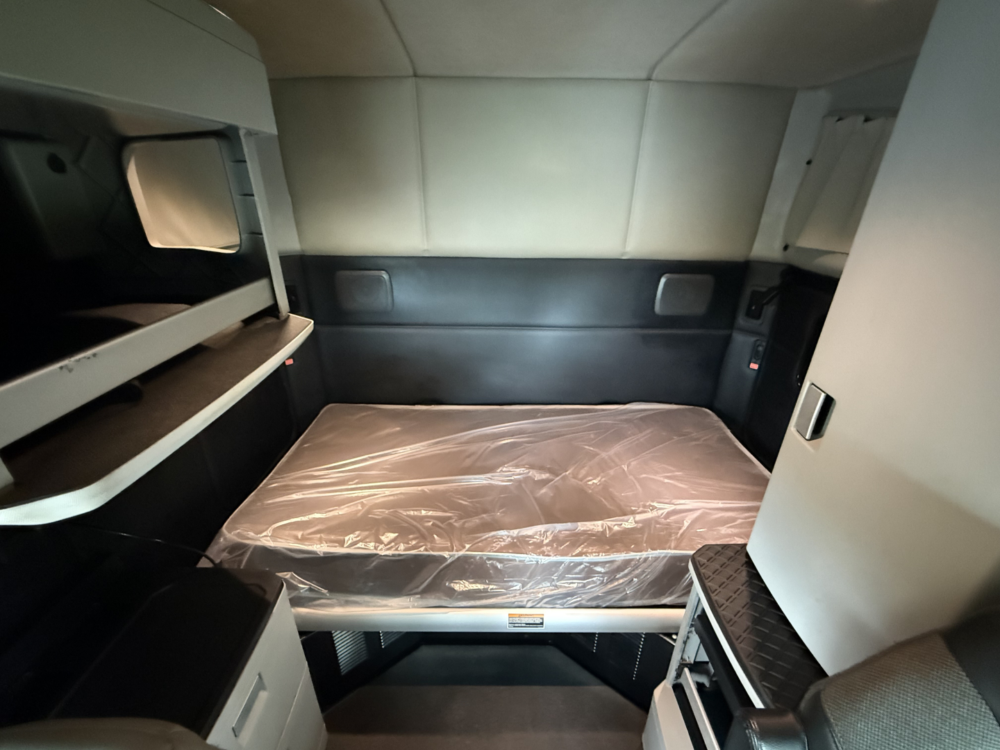 Kenworth T680 sleeper cab interior showing bed with plastic cover and surrounding storage compartments.
