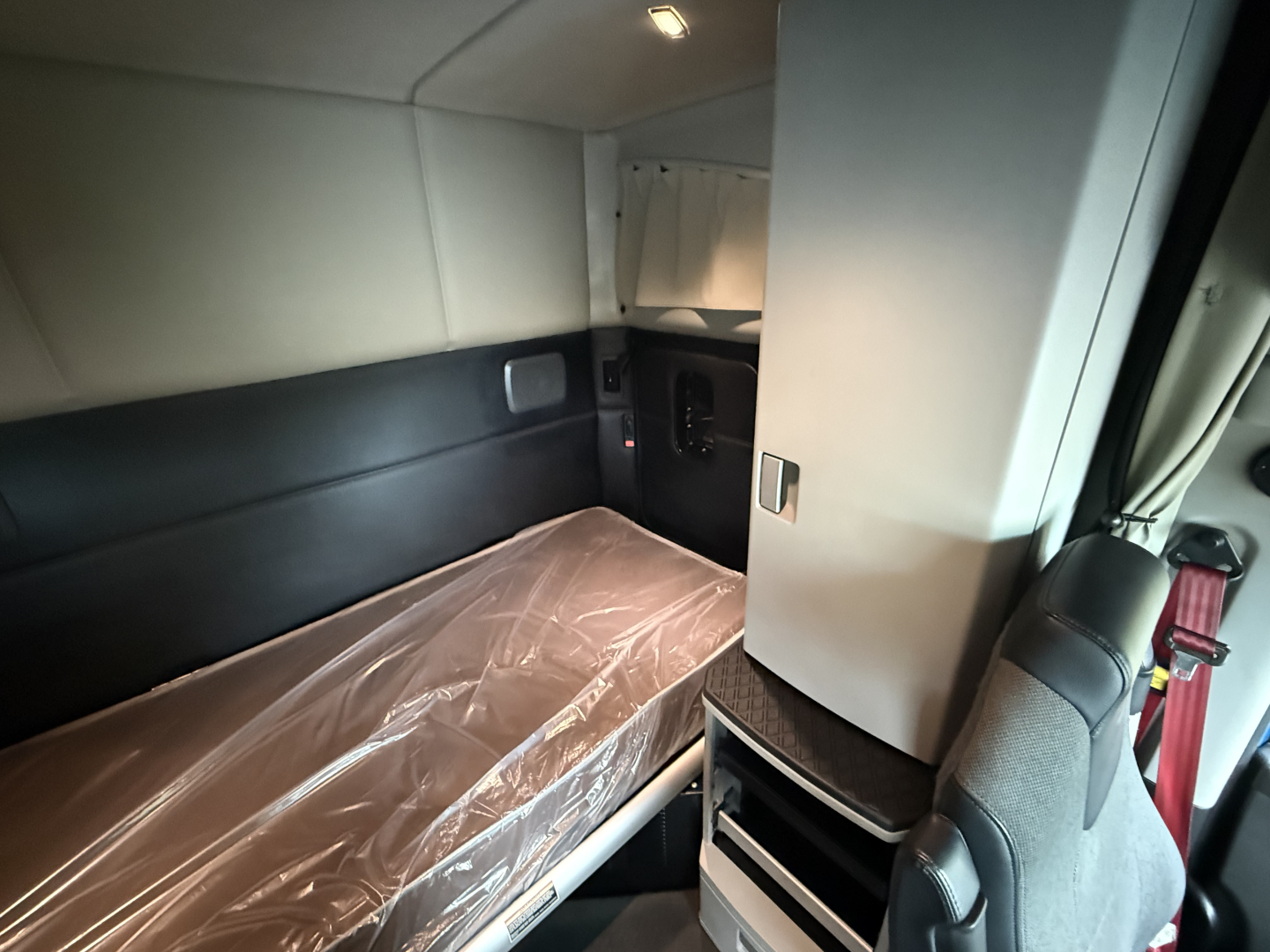 Kenworth T680 sleeper cab interior showing bunk bed with plastic cover and storage cabinet.