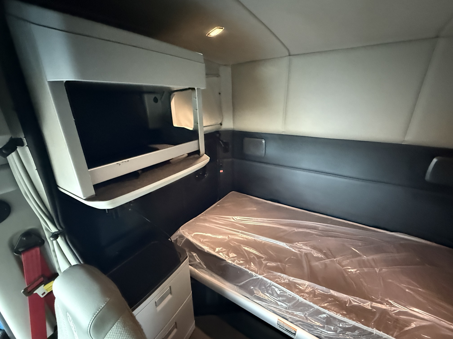 Kenworth T680 sleeper cab interior showing bunk bed with plastic cover and overhead storage shelf.