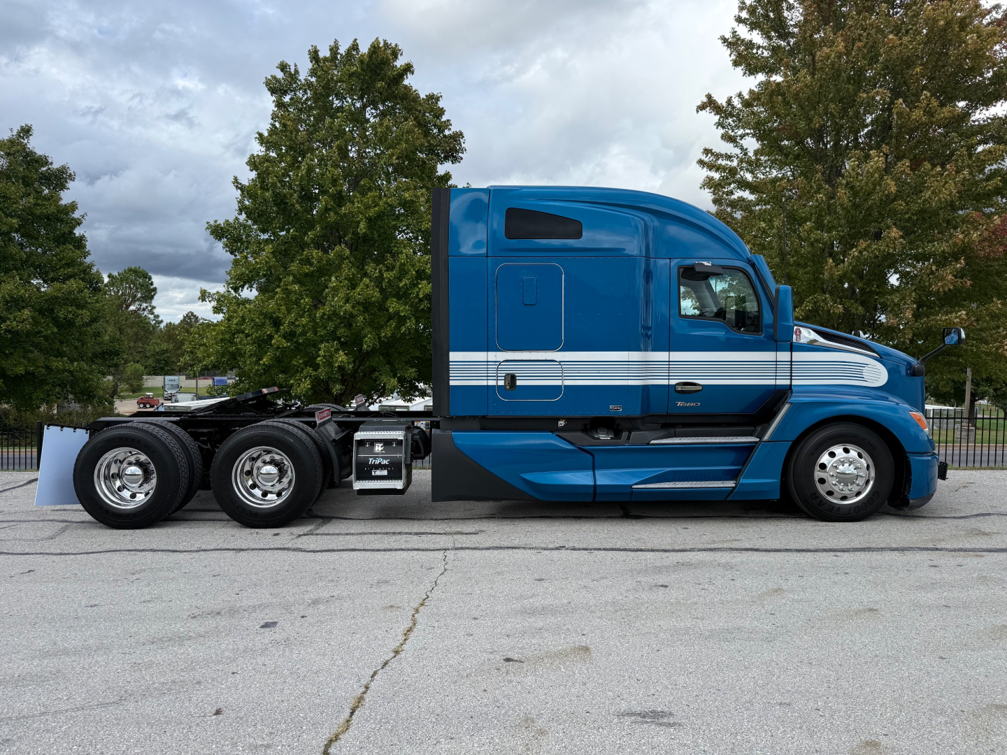 Kenworth T680 tractor in blue with sleeper cab, side view, showing dual rear axles and chrome wheels.